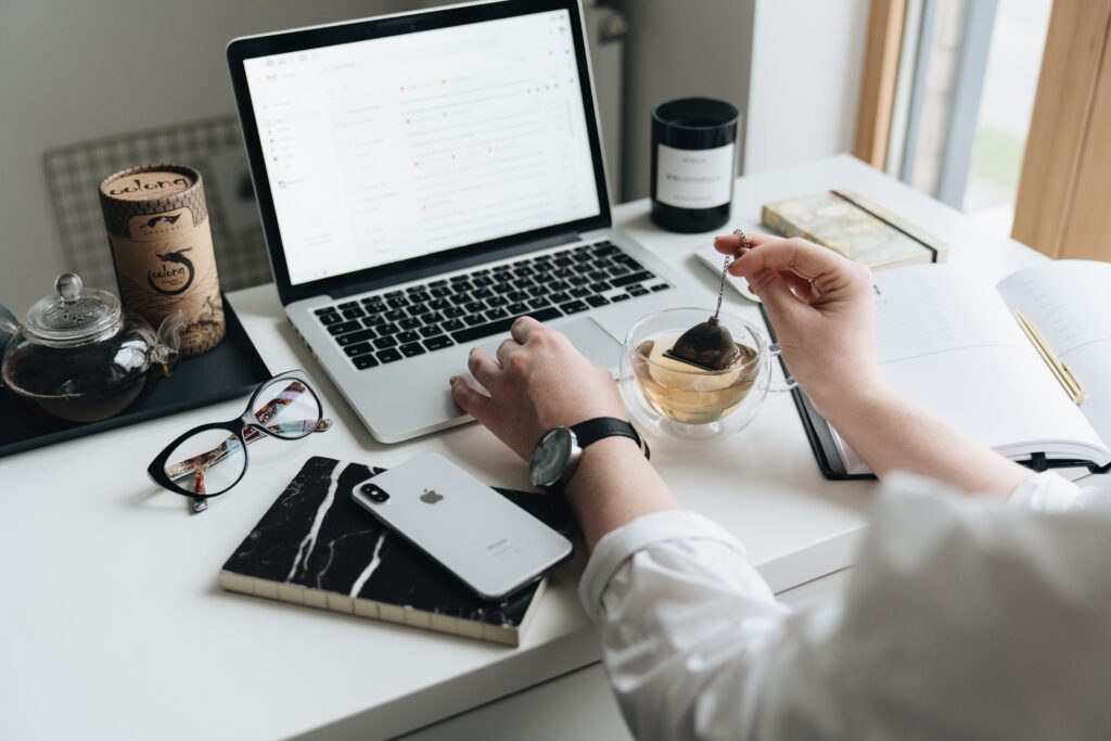 Person working from home with a laptop, a cup of tea, and a planner, embodying a productive home office environment.